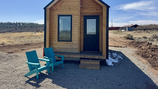 Une petite cabane en bois avec deux fenêtres et une porte, une chaise bleue et un sol recouvert de gravier.