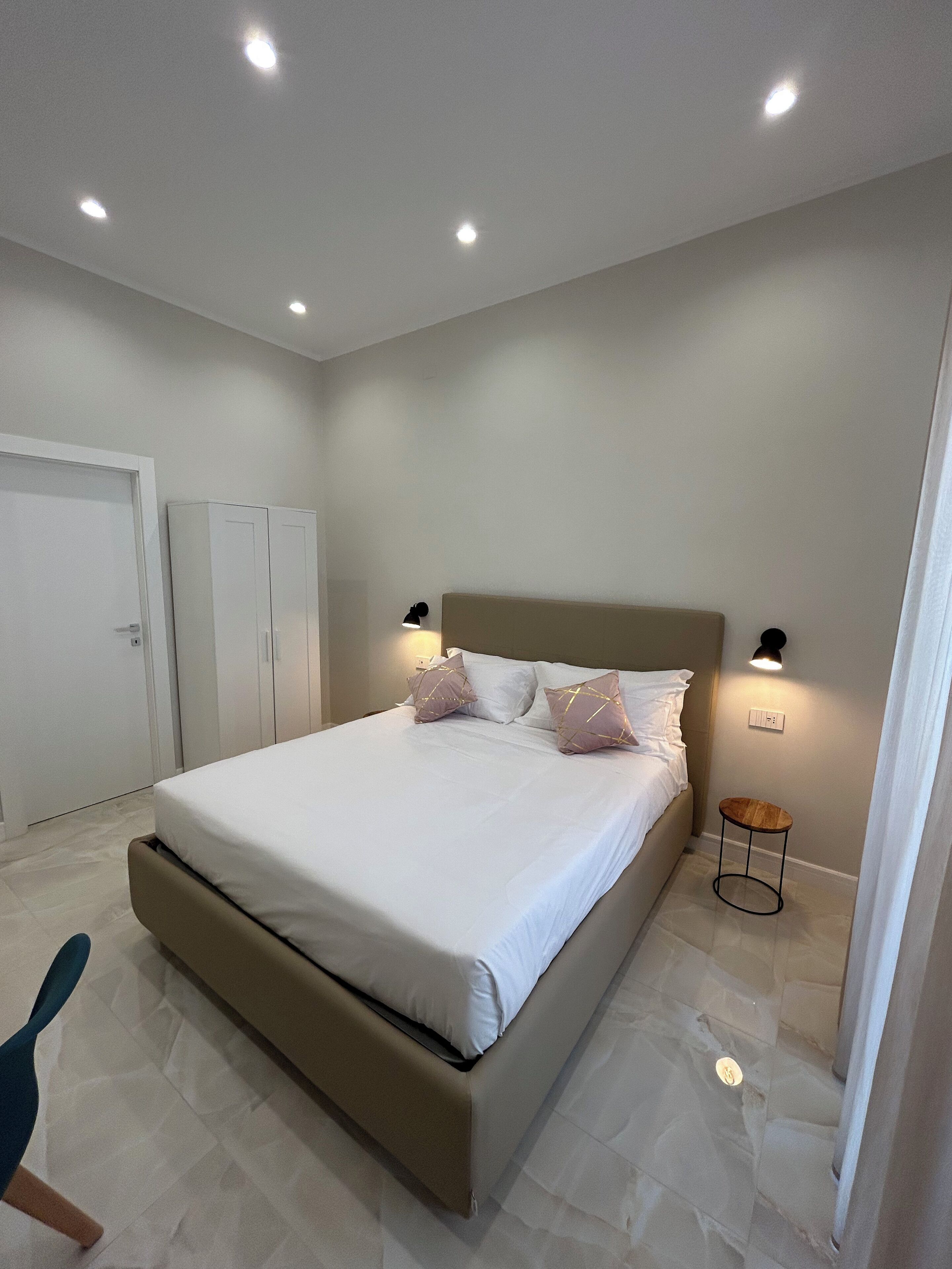 A bedroom with a bed, bedside lamps, a wardrobe, and a small round table.