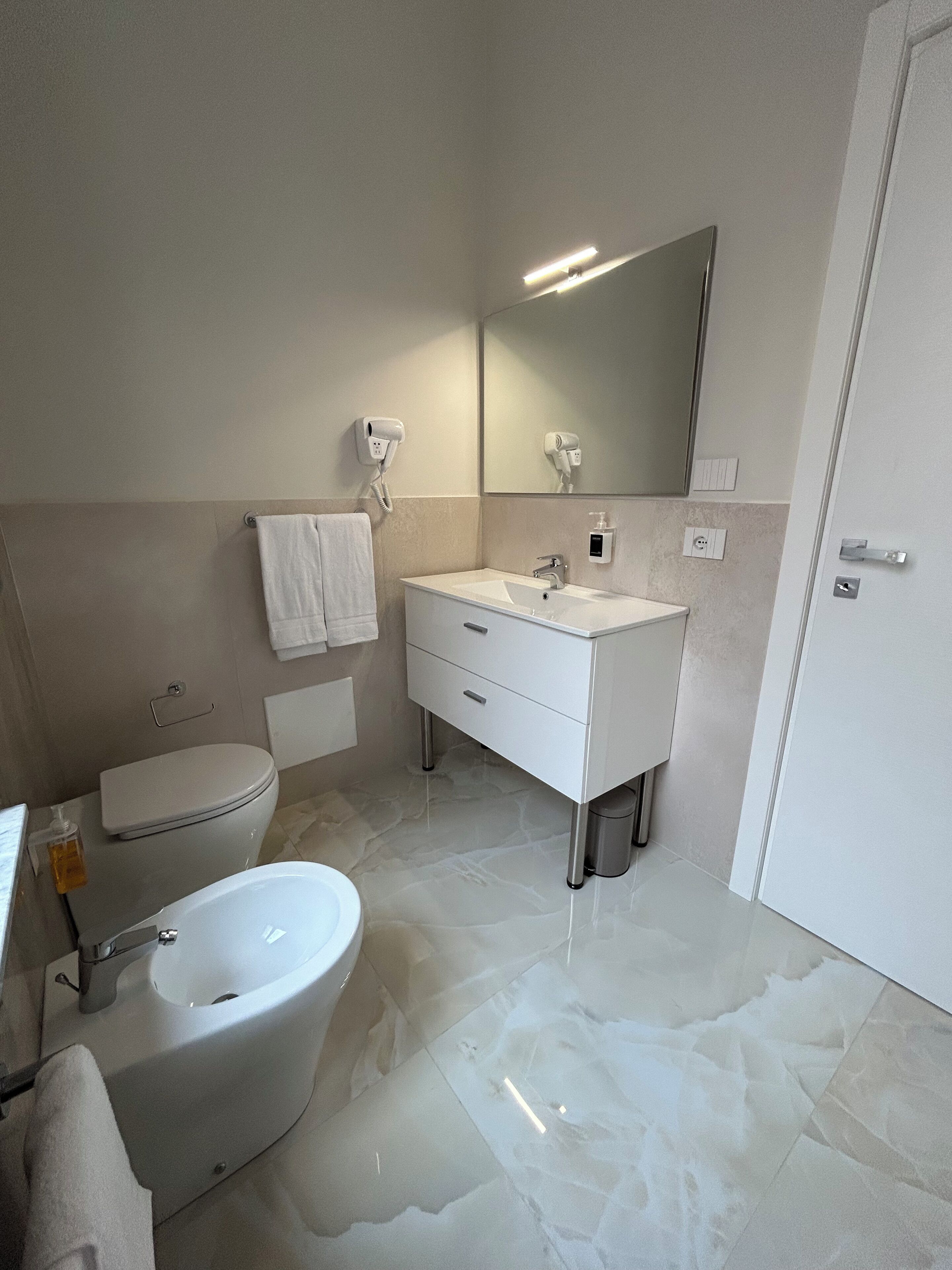 Un bagno moderno con una vasca freestanding, un water, un mobile lavabo con specchio e un asciugacapelli fissato alla parete.