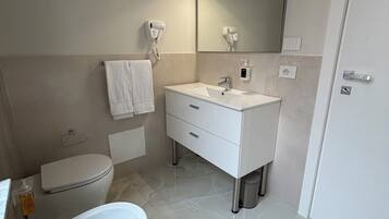 Un bagno moderno con una vasca freestanding, un water, un mobile lavabo con specchio e un asciugacapelli fissato alla parete.