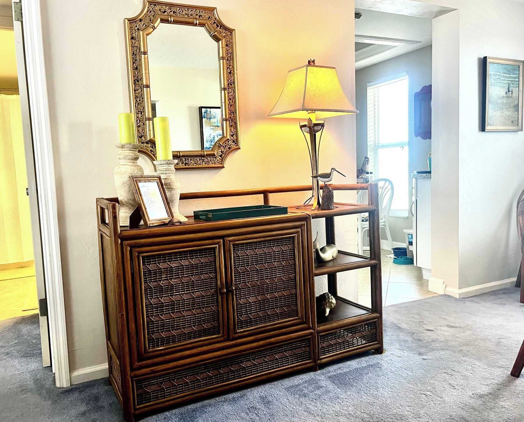 A wooden console table with a mirror and a lamp, a framed picture, and a small bird statue.