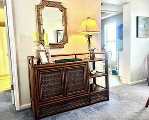 A wooden console table with a mirror and a lamp, a framed picture, and a small bird statue. - Island Reef #501 Beachfront Condo (Fort Myers Beach)