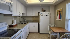 A compact kitchen with white cabinets, a microwave, a refrigerator, a stove, and a dining table with chairs.