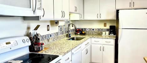 A kitchen with white cabinets, a microwave, stove, sink, and refrigerator.