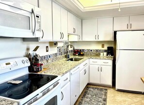A kitchen with white cabinets, a microwave, stove, sink, and refrigerator. - Island Reef #501 Beachfront Condo (Fort Myers Beach)