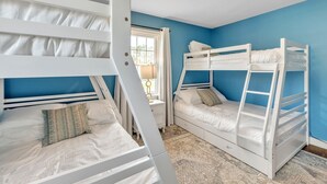 Een kamer met stapelbedden, een raam met gordijnen en een kamerkleed met een patroon.
