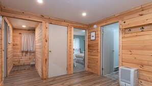 Ein Zimmer mit Holzwänden, einem Bett, einem Heizgerät und einer Tür zu einem weiteren Raum.