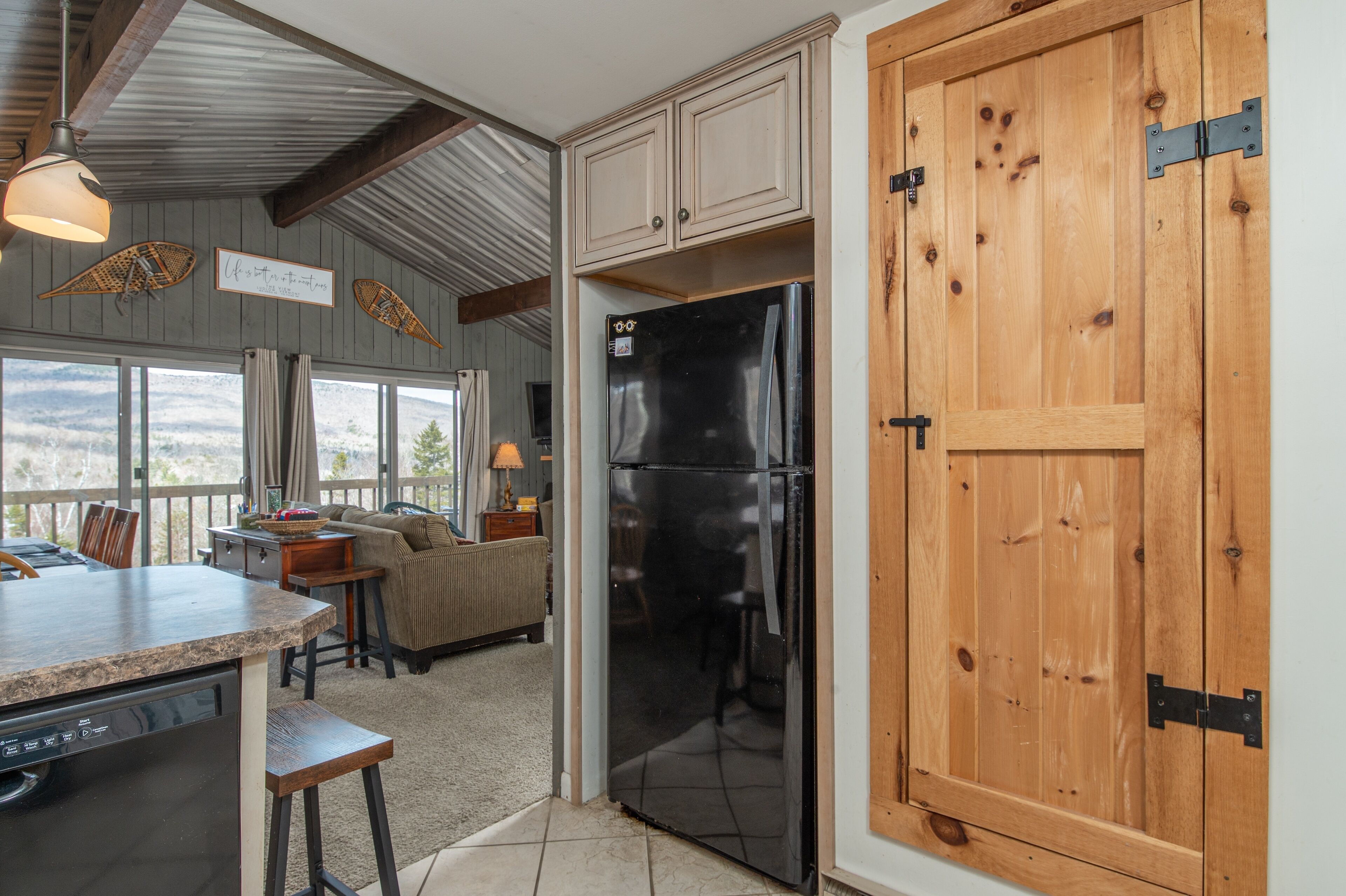 Une cuisine dotée d’un grand réfrigérateur noir, de meubles de rangement en bois et offrant une vue sur l’extérieur.