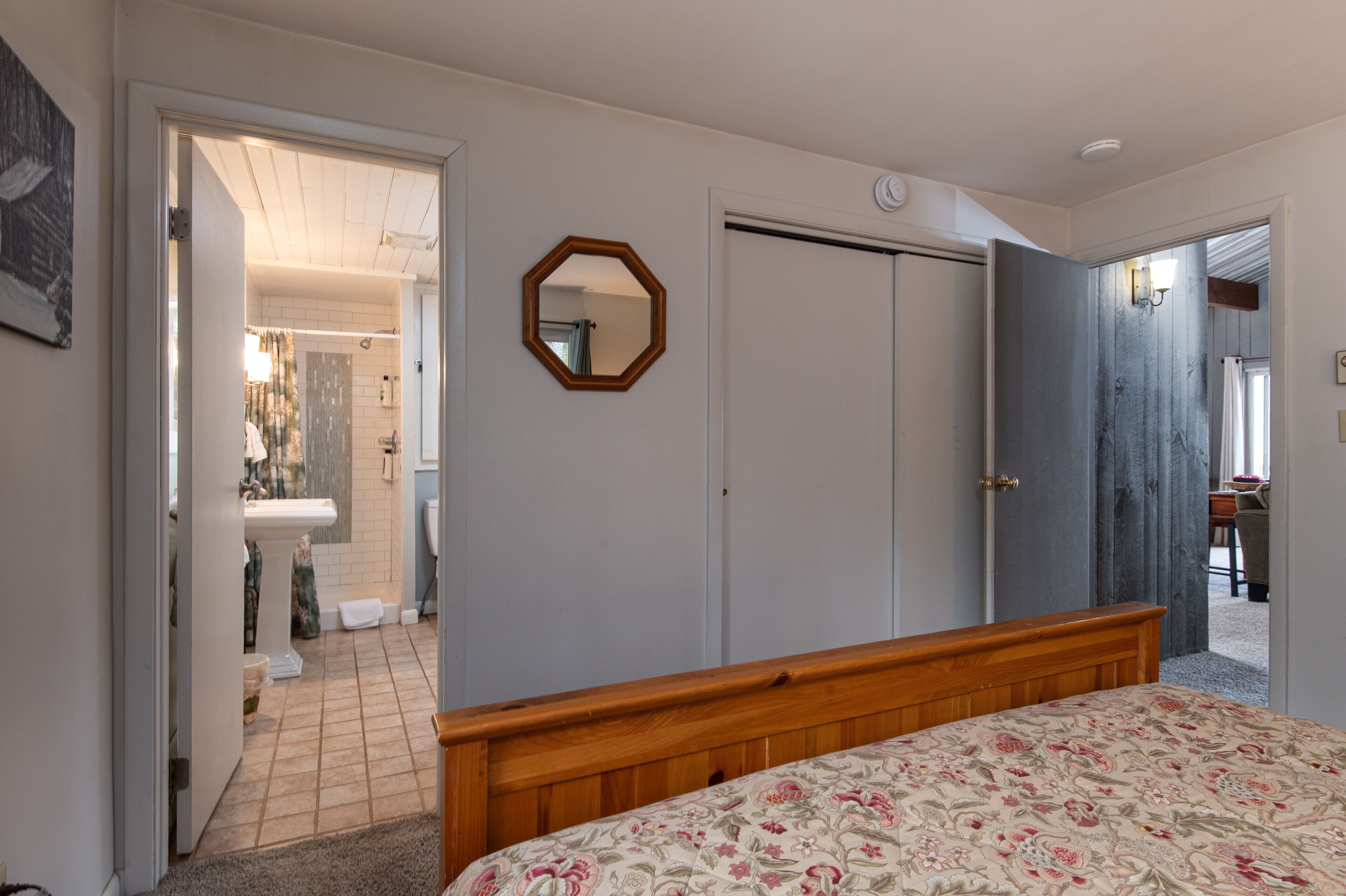A bedroom with a wooden bed, a mirror, and a wardrobe. There is a bathroom visible through an open door.