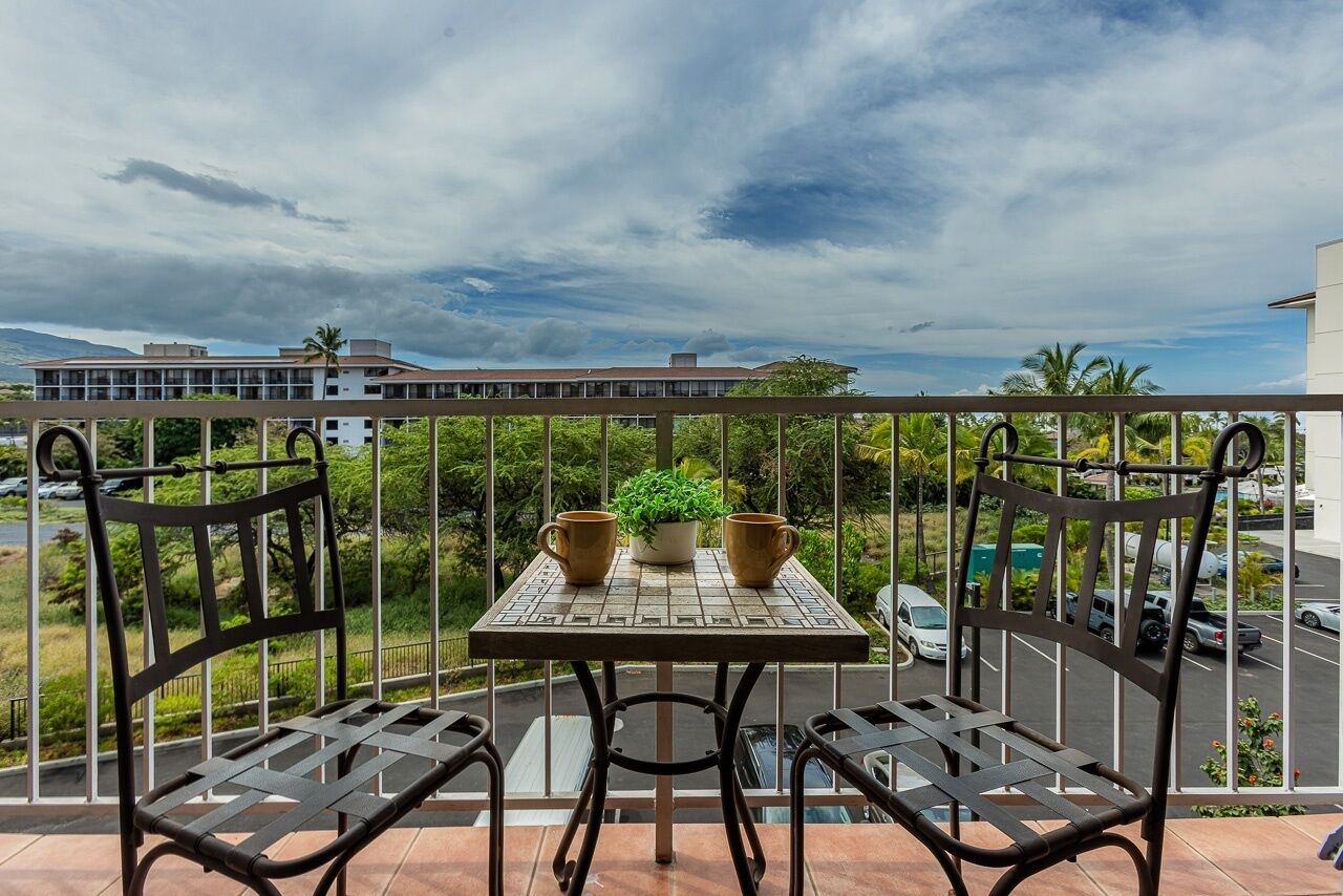 A balcony with two chairs and a table, a potted plant, and a view of buildings and greenery.