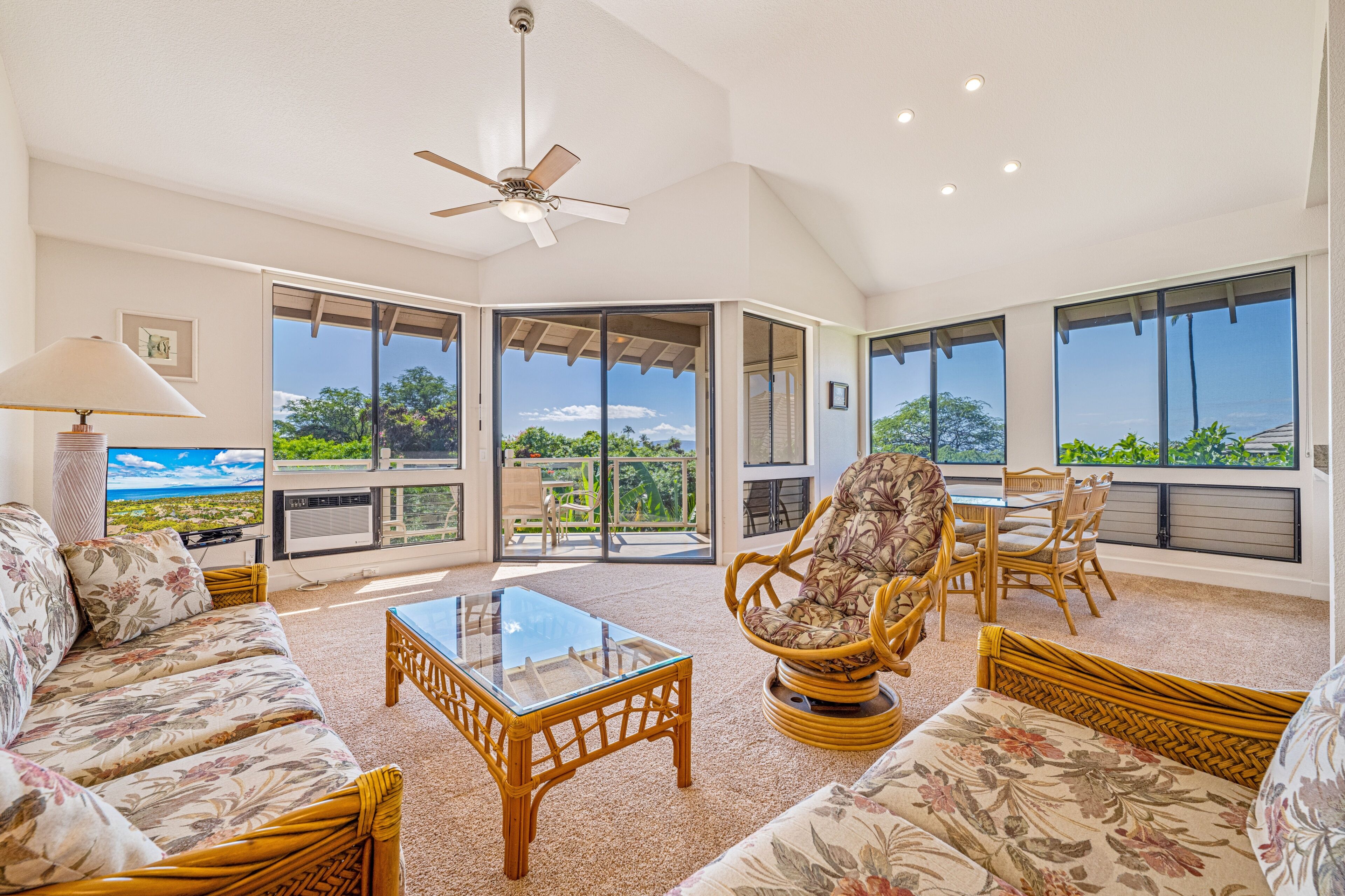 A spacious living area with a ceiling fan, a glass coffee table, and wicker furniture.