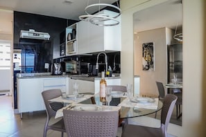A modern kitchen with a built-in microwave, toaster, and coffee maker. There is a dining area with a glass table and chairs, and a painting on the wall. - Beira Mar Fortaleza Landscape Platinum  (Fortaleza)