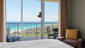 Une chambre d’hôtel dotée d’une grande porte-fenêtre coulissante donnant sur un balcon avec vue sur l’océan et une zone de villégiature.