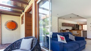 A modern living room with a blue sofa, wicker chairs, and a glass door leading to a kitchen. - Bz40 Casa 180m praia piscina privativa (Buzios)