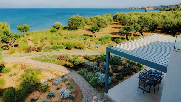Una terraza con vistas al mar, rodeada de vegetación y un comedor.