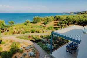 A terrace with a view of the sea, surrounded by greenery and a dining area.