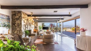 Una sala de estar moderna con chimenea de piedra, asientos cómodos, un televisor de pantalla plana y un amplio ventanal que da a un espacio exterior.