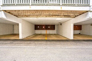 Un garage souterrain avec deux places de stationnement, une ligne jaune qui marque le centre, et des armoires en bois au fond.