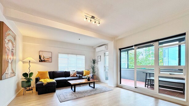 A spacious living room with a dark-colored sofa, a wooden coffee table, and a large sliding glass door leading to an outdoor area.