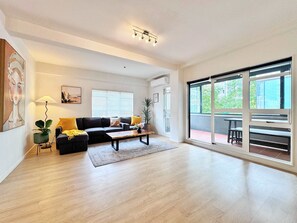 Un salon spacieux avec un canapé aux couleurs sombres, une table basse en bois et une grande porte-fenêtre coulissante donnant sur un espace extérieur.