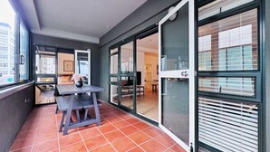 A balcony with a table and chairs, a potted plant, and a sliding glass door leading to an interior space.