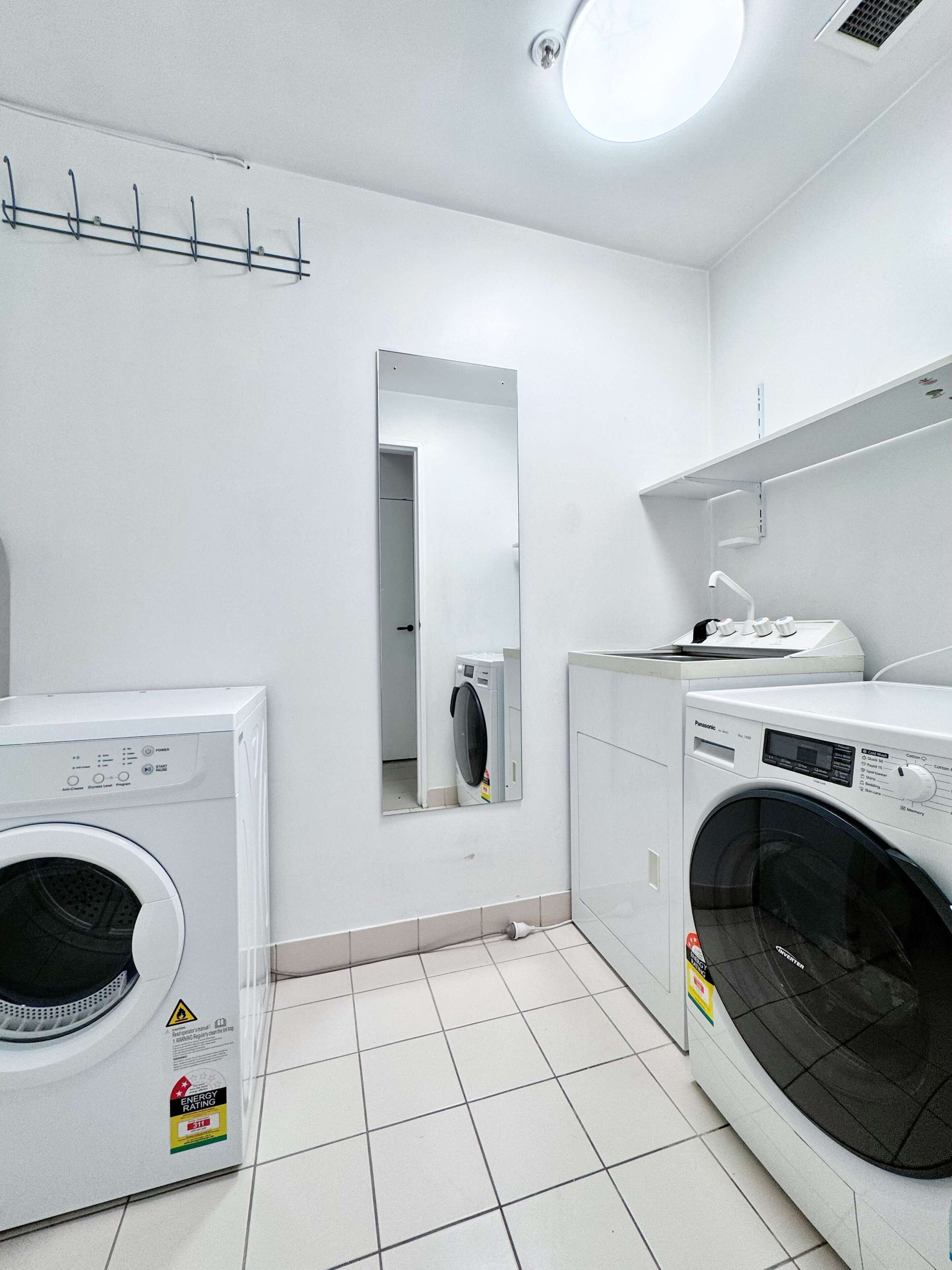A laundry room with two washing machines, a mirror, and a shelf with a faucet.