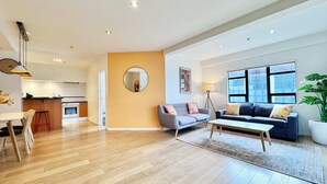 A modern living room with a sofa, coffee table, and a dining area with chairs. - Heart of Auckland 2BR Near Queen St & Skytower (Auckland)