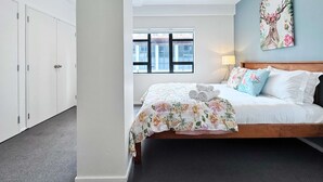 A bedroom with a bed, a window, a door, and a wall with a floral painting.