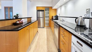 A modern kitchen with wooden cabinets, stainless steel appliances, and a black countertop. - Heart of Auckland 2BR Near Queen St & Skytower (Auckland)