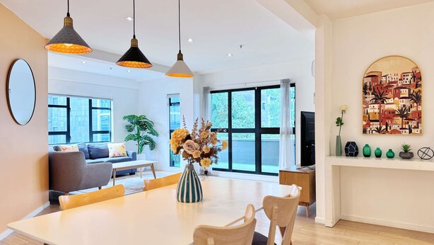 A modern living room with a dining area, large windows, and a view of the city.