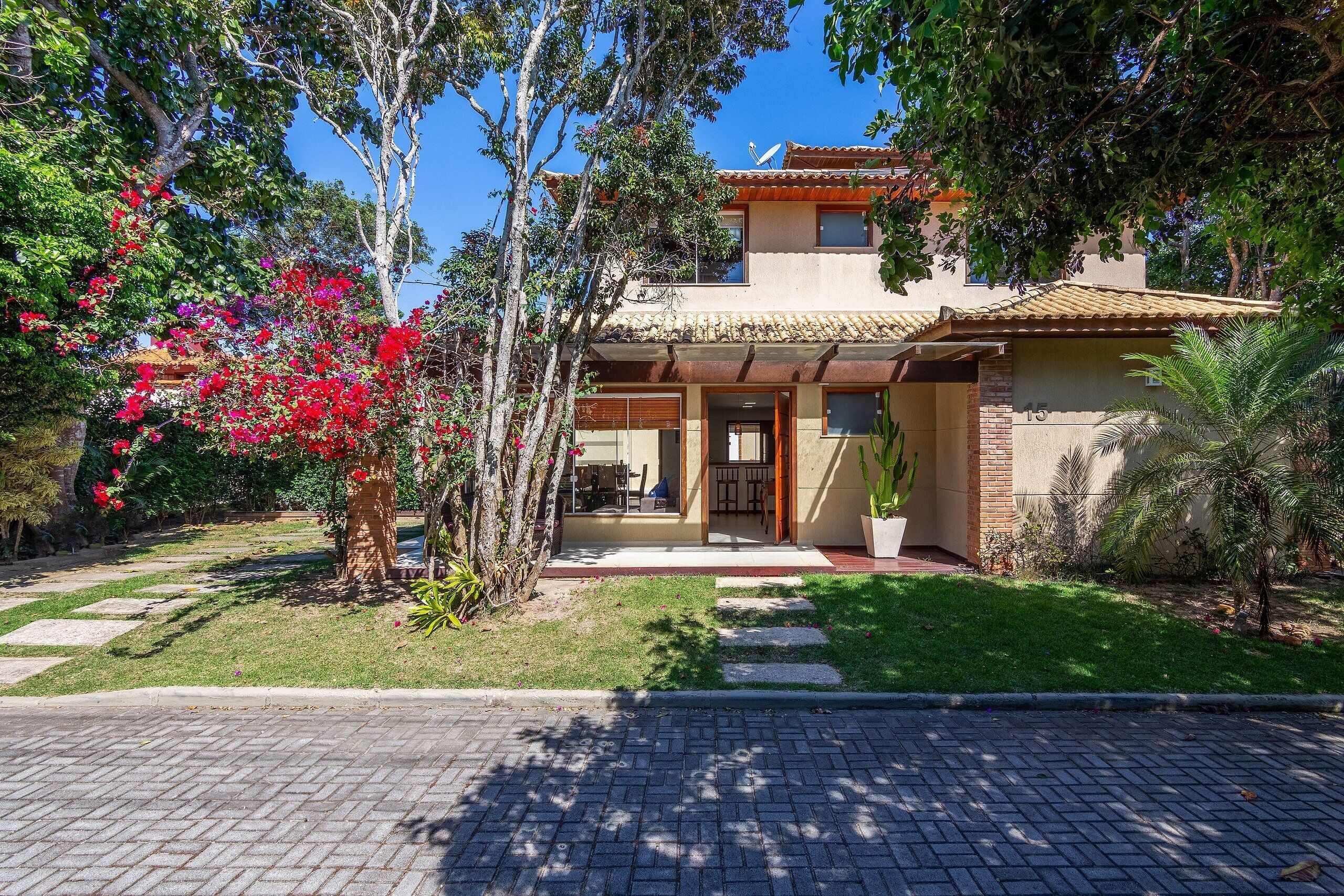 A two-story house with a tiled roof, a covered porch, and a well-maintained garden with red flowers and a small tree.