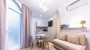 A modern living room with a sofa, dining table, and chairs. There is a kitchen area with cabinets and a stove. The room has a large window with curtains. - Madeleine Opera - Very nice Studio in Paris (Paris)