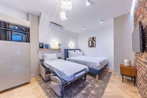 A modern bedroom with two beds, a built-in wardrobe, a flat-screen TV, and a brick accent wall. - Madeleine Opera - Very nice Studio in Paris (Paris)