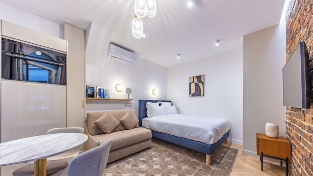 A modern bedroom with a bed, a sofa, a dining table, and a TV. - Madeleine Opera - Very nice Studio in Paris (Paris)