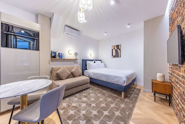 A modern bedroom with a bed, a sofa, a dining table, and a TV.