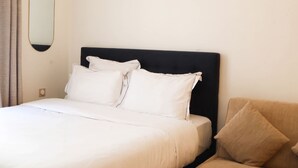 A hotel room with a bed, two pillows, a headboard, a wall-mounted mirror, and a beige sofa.