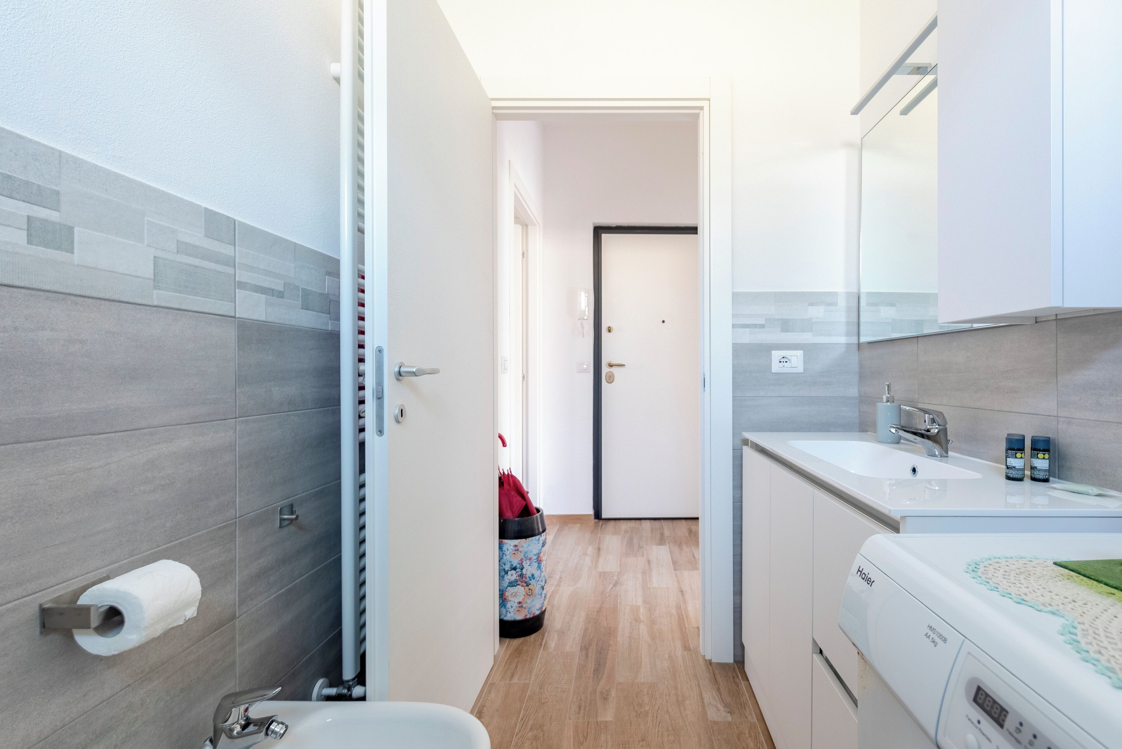 Ein modernes Badezimmer mit grauen Fliesen, einer Toilette, einem Waschbecken und einer Waschmaschine.