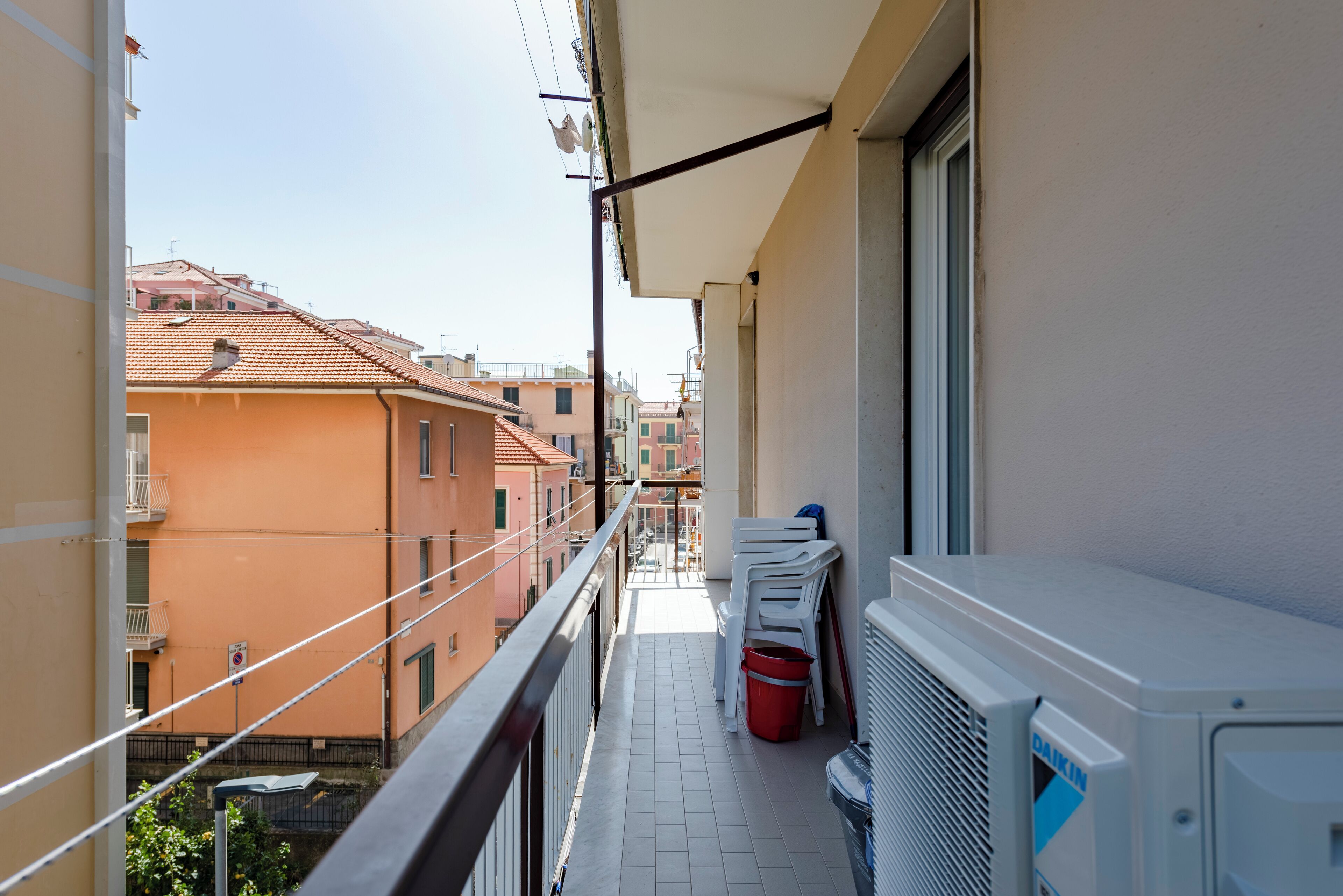 A balcony with a white air conditioning unit, a red bucket, and stacked white chairs.