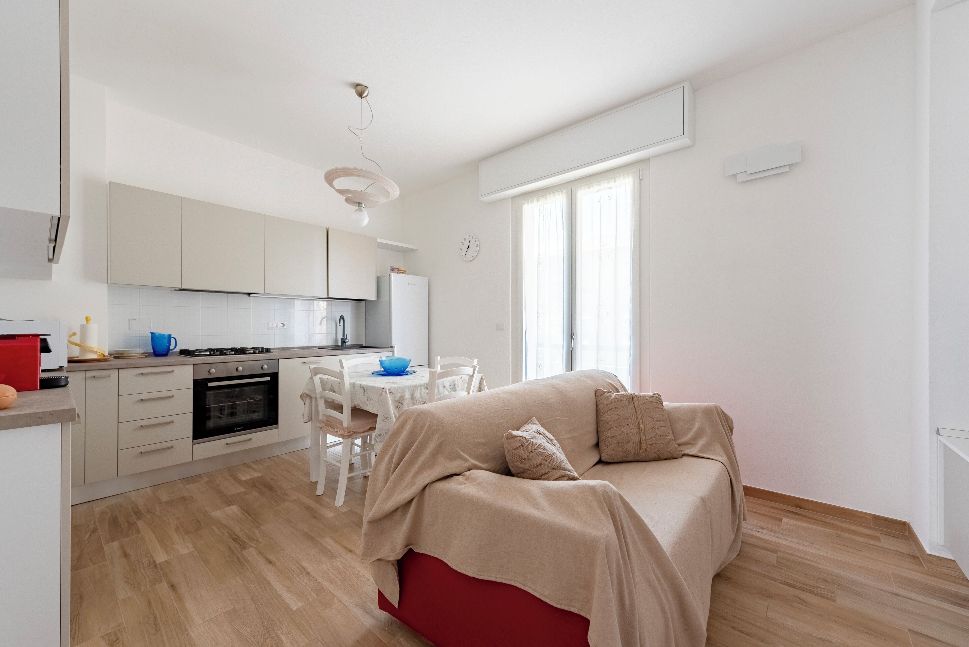 A modern kitchen with white cabinets, a red sofa, and a dining area with a white table and chairs.