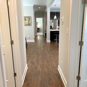 Un corridoio con pavimento in legno che conduce a una zona cucina con frigorifero e lampada a sospensione.