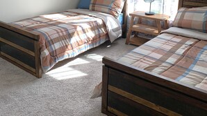 Une chambre à coucher avec deux lits en bois, une petite table de chevet et une fenêtre avec des rideaux.