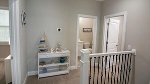 Een gang met een witte console tafel, een model zeilboot en een beeld van een vogel. Een deur leidt naar een badkamer met een toilet en een ingelijste foto aan de muur.