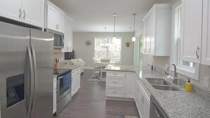 Een moderne keuken met witte kasten, roestvrijstalen apparatuur, granieten aanrechtbladen en hanglampen.