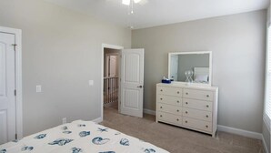 Een slaapkamer met een bed, een ladekast, een spiegel en een plafondventilator.