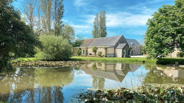 A stone building with a pond in front, surrounded by trees and greenery.