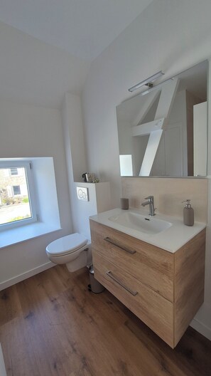 A modern bathroom with a wooden vanity, a large mirror, and a window providing natural light.