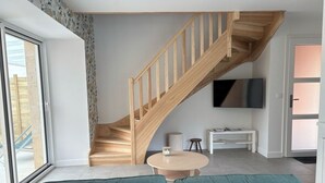 A modern living room with a wooden staircase, a round table, and a teal sofa.