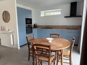 A modern kitchen with blue cabinets, a round wooden table, and a black range hood.