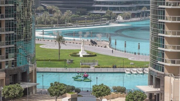 A modern hotel with a central courtyard featuring a fountain, palm trees, and a statue.