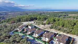 Zona residencial com várias casas, cercada por vegetação e montanhas ao fundo.